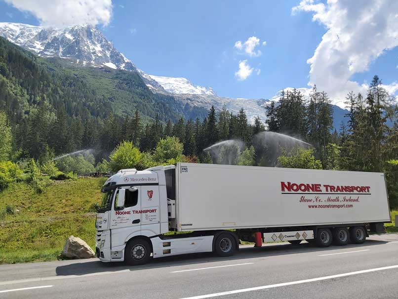 A Noone Transport and Logistics Truck driving alongside some snowy mountains